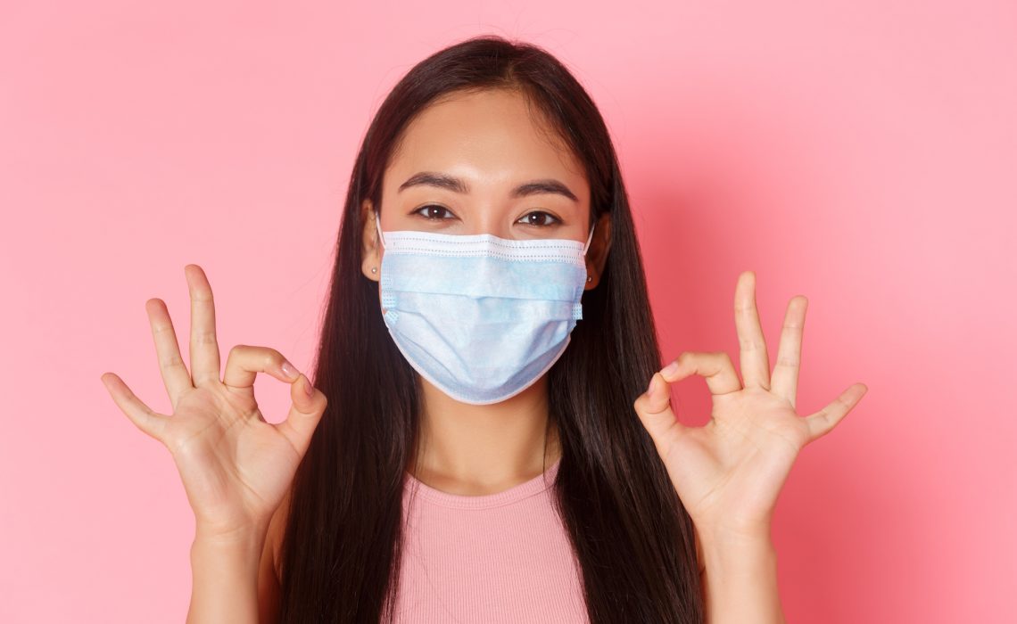 Covid-19 pandemic, coronavirus and social distancing concept. Close-up of excited and amazed pretty asian girl praise great choice, well done or good job gesture, show okay and wear medical mask.