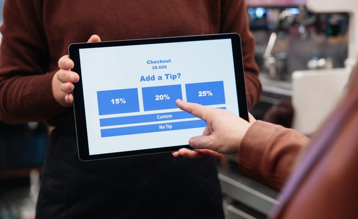 Employee holding tablet for tip payment in cafe and customer touching it to pay tip