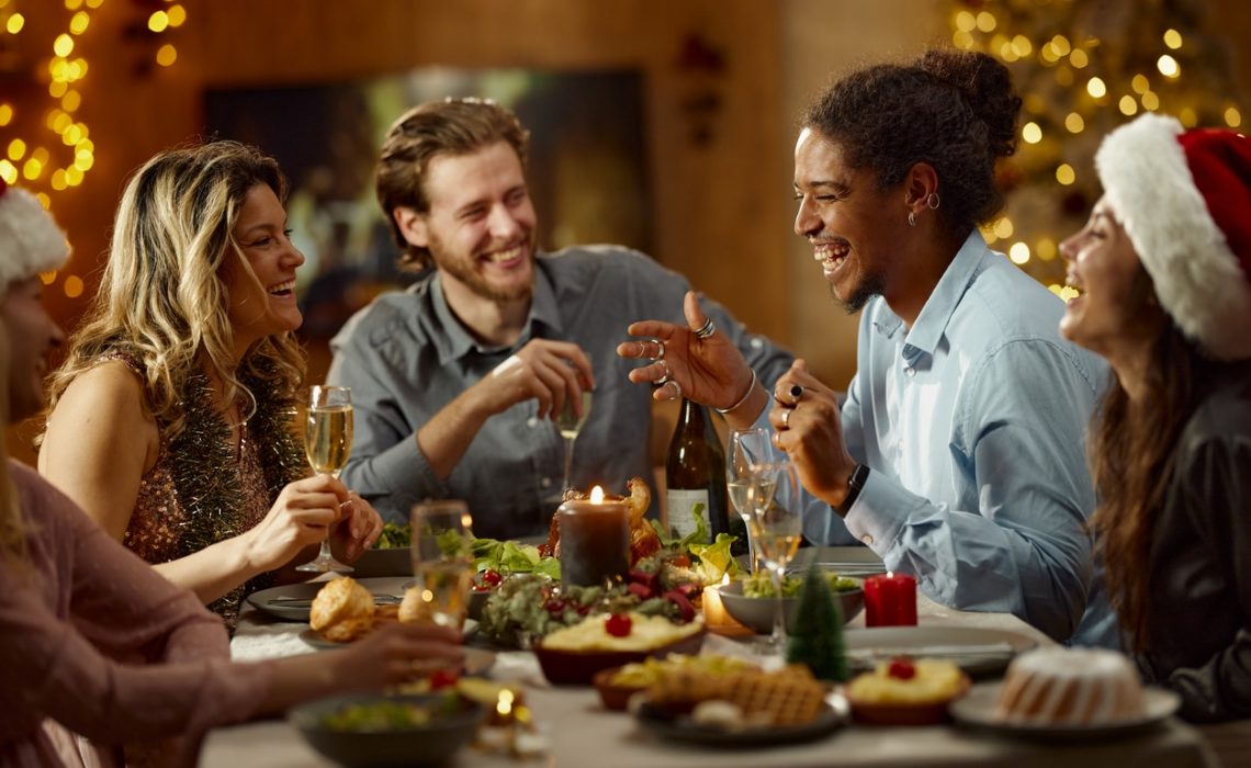 Cheerful diverse friends communicating while enjoying in lunch on New Year's day at home. Focus is on black man and woman across him.